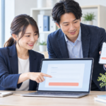 ノートパソコンとスマートフォンで問い合わせフォームを確認する中小企業の担当者